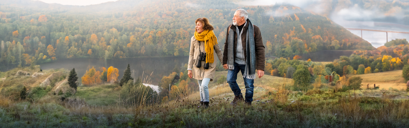 An older couple walking through an autumnal field wearing arthritis supports under their clothes