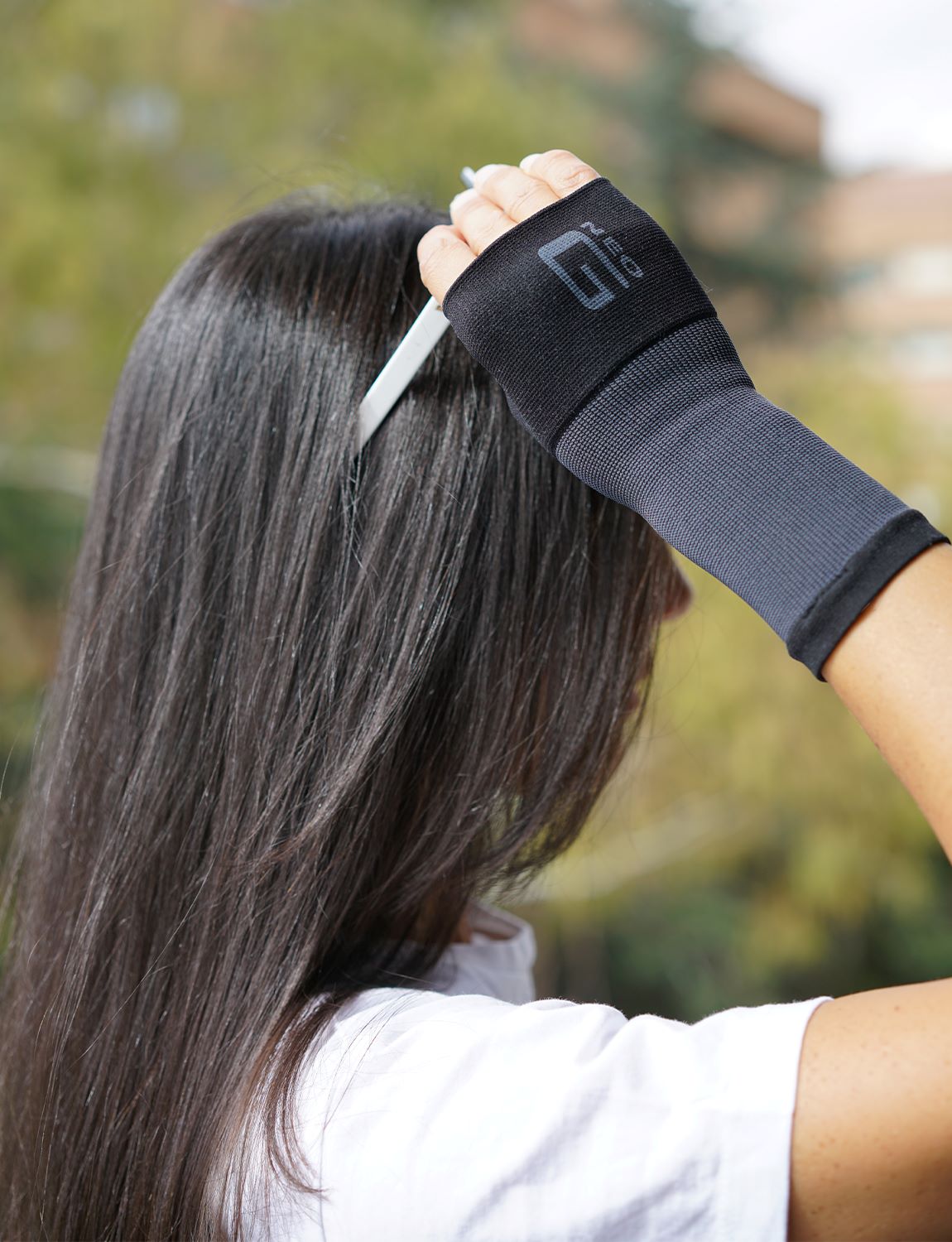 Woman wearing black Neo G Airflow Wrist & Thumb Support on right hand, adjusting sunglasses