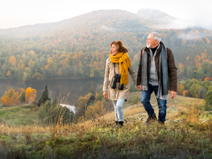 An older couple walking through an autumnal field wearing arthritis supports under their clothes