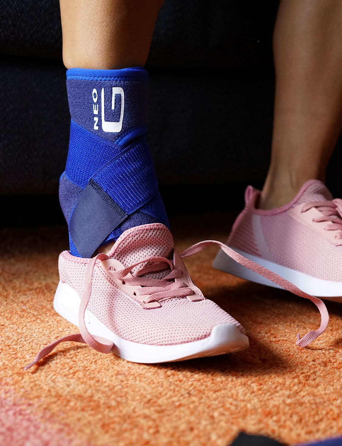 Woman wearing Neo G Ankle Support with Figure of 8 Strap putting on pink trainers