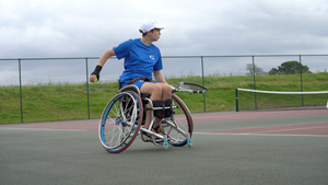 Ellen Tribley on a tennis court with a cloudy sky, about to serve. 